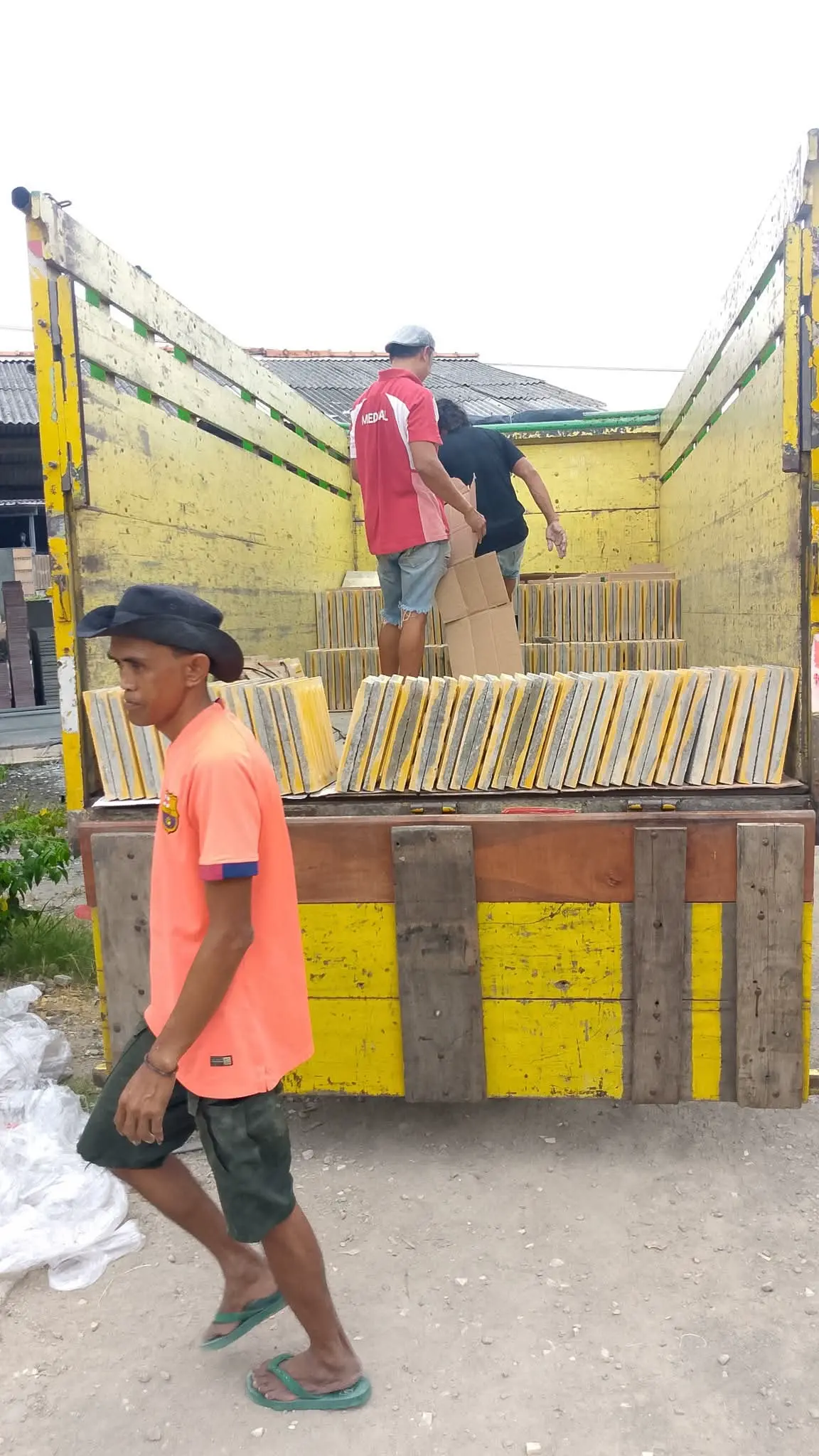 Pekerja sedang memuat ubin guiding block kuning ke dalam truk pengiriman